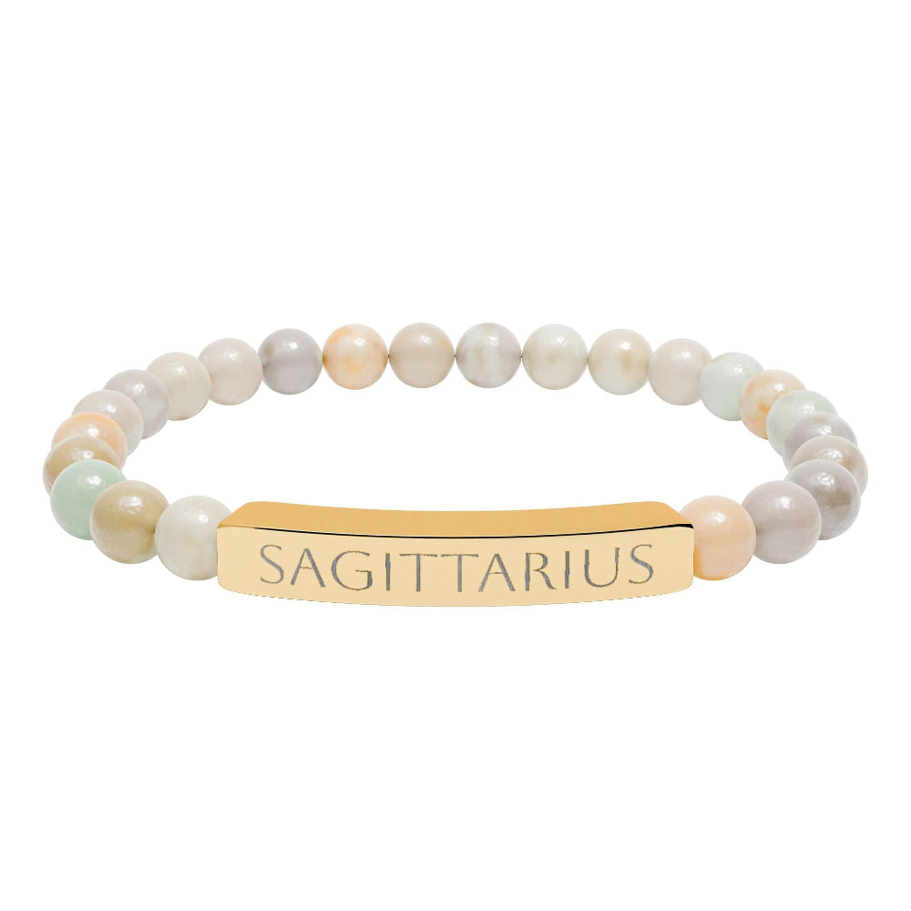 Bracelet with polished pastel beads in soft peach, cream, gray, and light blue tones with natural marbling, featuring a gold-plated curved bar engraved "SAGITTARIUS" in uppercase letters. Stretch-fit zodiac-inspired crystal jewelry.