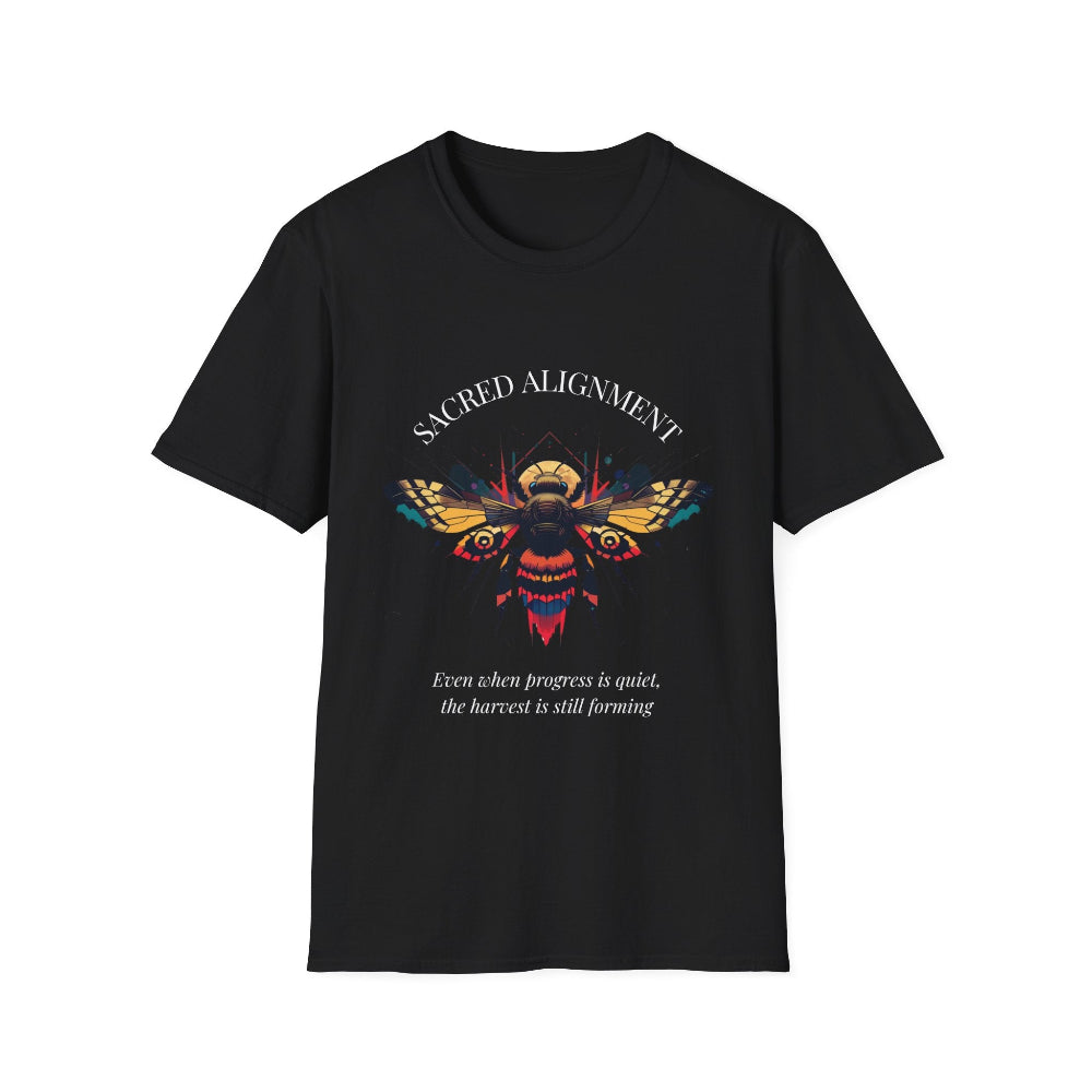 Black unisex cotton t-shirt laid out flat featuring bold "Sacred Alignment" graphic: vibrant abstract bee with detailed wings and body, colorful geometric accents, and dynamic paint splatters in red, orange, teal, blue, and gold tones bursting outward around an orange moon background. Arched white text "SACRED ALIGNMENT" above and smaller inspirational quote "Even when progress is quiet, the harvest is still forming" below. Motivational spiritual empowerment crewneck tee.