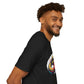 Black unisex cotton t-shirt in side profile on smiling male model with curly hair and beard, featuring bold Cancer zodiac graphic on chest: vibrant abstract crab portrait with large claws, intense eyes, symmetrical geometric shell patterns, and dynamic multicolored paint splatters in gold, red, navy, teal, and black tones exploding outward. Elegant white cursive "Cancer" text below. Astrology zodiac motivational crewneck tee.