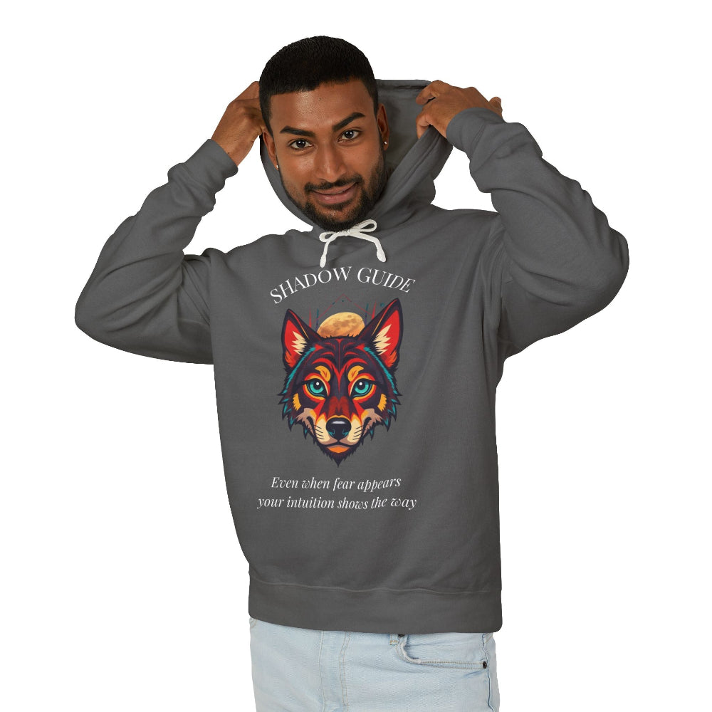 Young man with short hair pulling up the hood of a dark gray hoodie featuring vibrant multicolored wolf head graphic, intense eyes in orange blue teal splashes, full moon above, "SHADOW GUIDE" arched text, motivational quote about intuition and fear below
