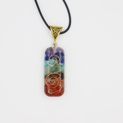 Rectangular orgonite pendant necklace in clear resin with embedded healing gemstones (turquoise, carnelian, amethyst, lapis) and copper spiral wire design, gold engraved triangular bail on black cord, spiritual energy jewelry on white background