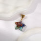 Star-shaped orgonite pendant necklace in clear resin with embedded healing gemstones (turquoise, carnelian, amethyst, lapis) and central copper spiral, gold engraved triangular bail, displayed on white wavy marble background