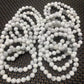 White howlite round gemstone bead strands with natural gray veining, polished marble-look beads displayed on a dark woven textured surface.