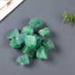 Close-up of raw green fluorite crystals: cluster of translucent emerald-green rough stones with natural cubic shapes, glassy luster, subtle internal clarity, and light reflections, scattered on a dark gray background with fern leaf accent. Natural healing gemstone for heart chakra, emotional balance, and mental clarity.